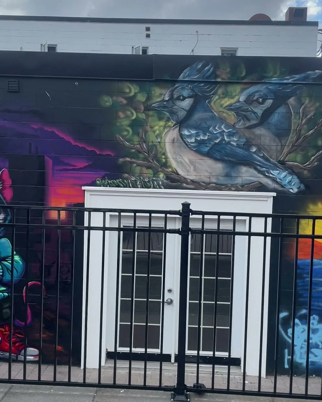 Completed Blue Jays mural above a doorway with portions of adjacent artists' mural sections visible on both sides